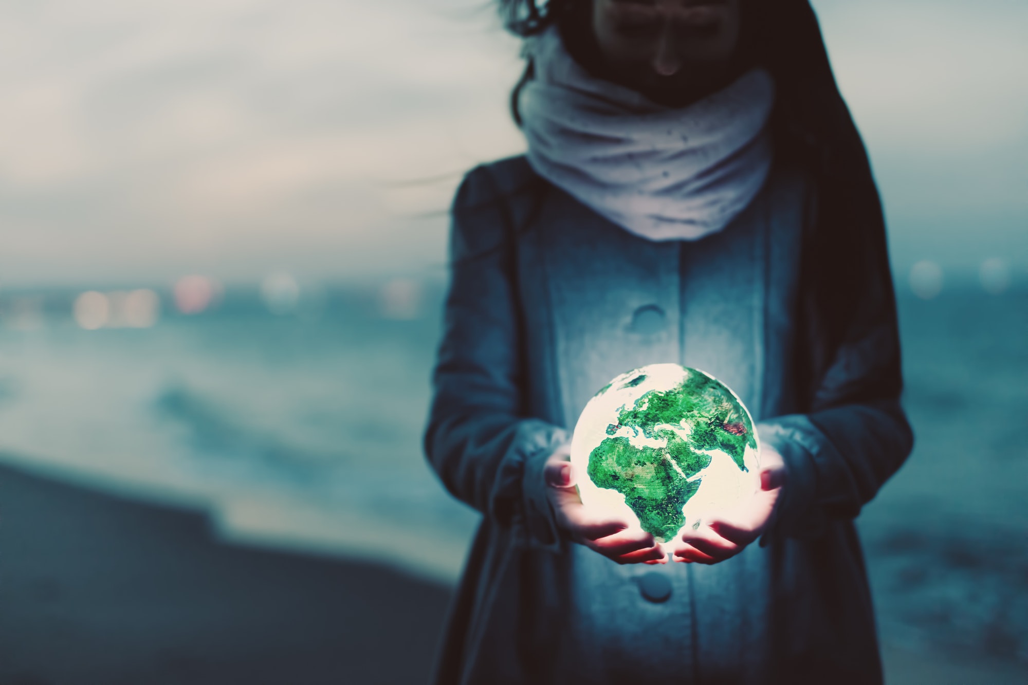 Earth globe glowing in woman's hands on the beach at night.
