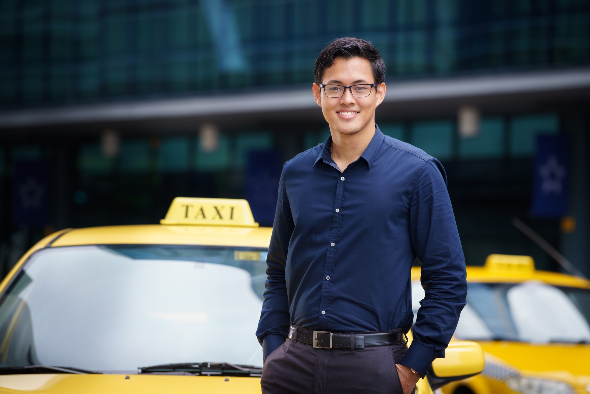 Portrait of happy chinese taxi driver leaning on yellow car with arms crossed, smiling and looking at camera by diego_cervo