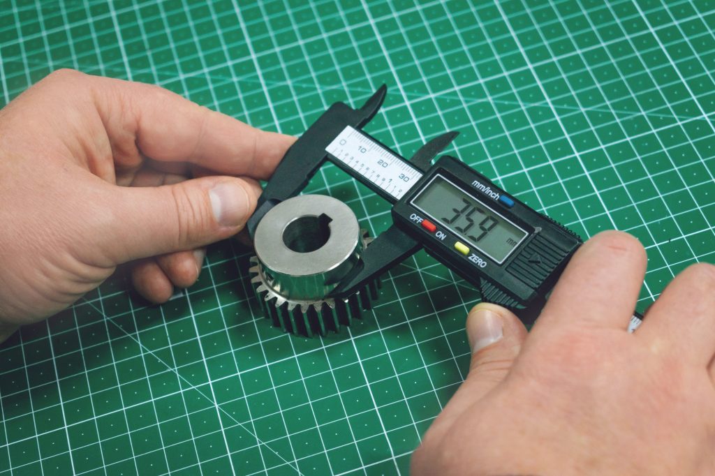 Metal gear measurement process. Factory man, worker measuring steel detail, gear with digital